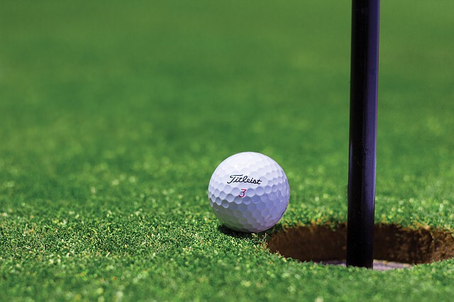 White golf ball on green next to hole with black flag