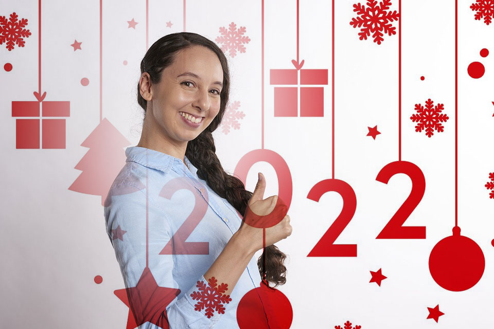 Young person with braided hair smiling at camera in front of holiday-themed backdrop with festive decorations